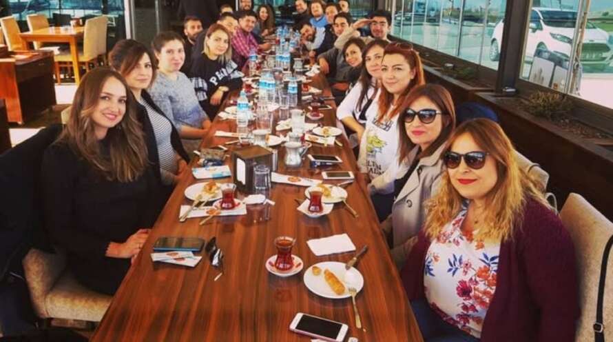 Yavuz Usta Oltu Cağ Kebabı restoranında, uzun bir masada bir grup insan masada tatlı ve çay eşliğinde fotoğraf çekiniyor.